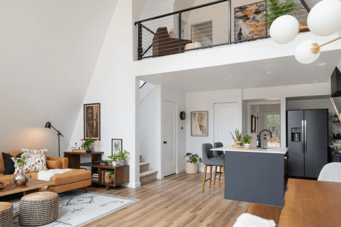 Modern living space with a cozy sofa, plants, and a kitchen area featuring a black fridge and wooden accents.